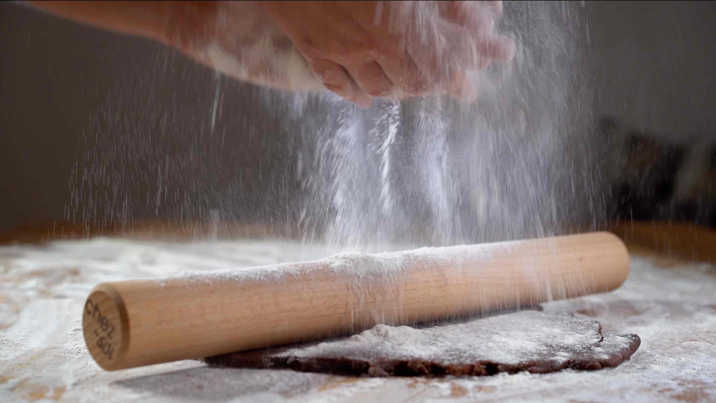 Hand streut Mehl auf Nudelholz
